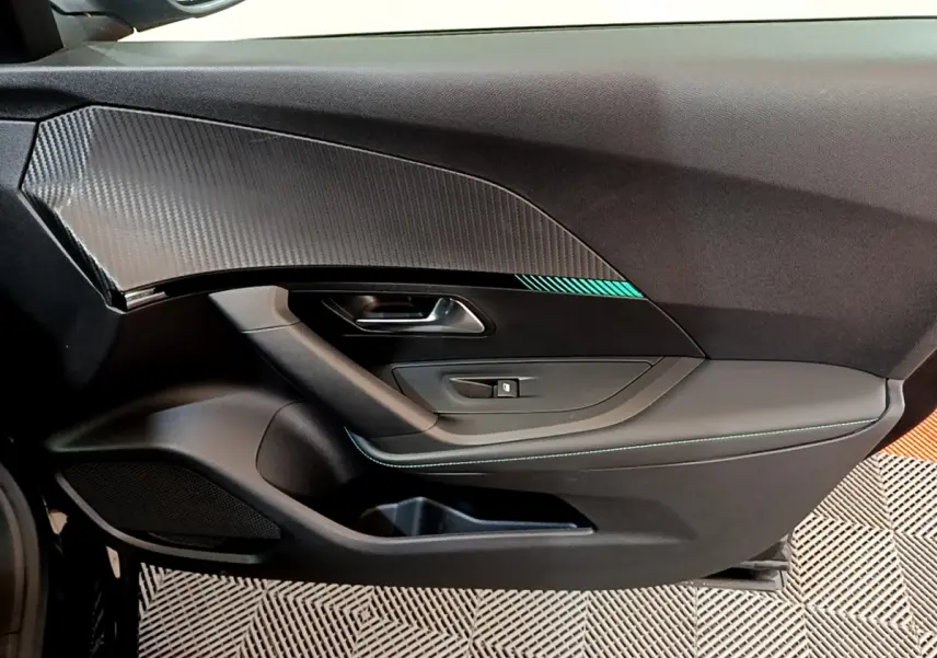Vue intérieure côté gauche de la porte noire du Peugeot 2008 PureTech 130 avec insert carbone et surpiqûres bleues.