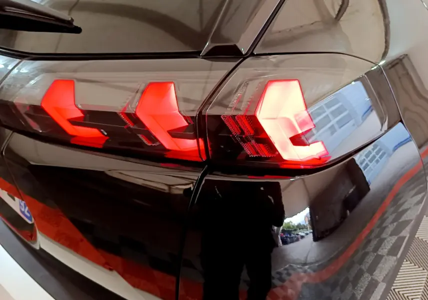 Gros plan sur le feu arrière droit rouge vif d'un Peugeot 2008 noir brillant, reflet d'un garage visible.