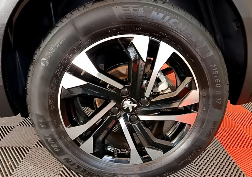 Gros plan sur la roue avant droite du Peugeot 2008 noir, mettant en valeur la jante alliage bicolore et le pneu Michelin.