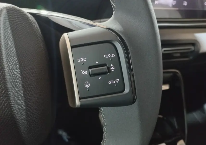 Gros plan sur les commandes gauche du volant cuir gris foncé de la Citroën C3 hybride 2025, avec boutons multifonctions.