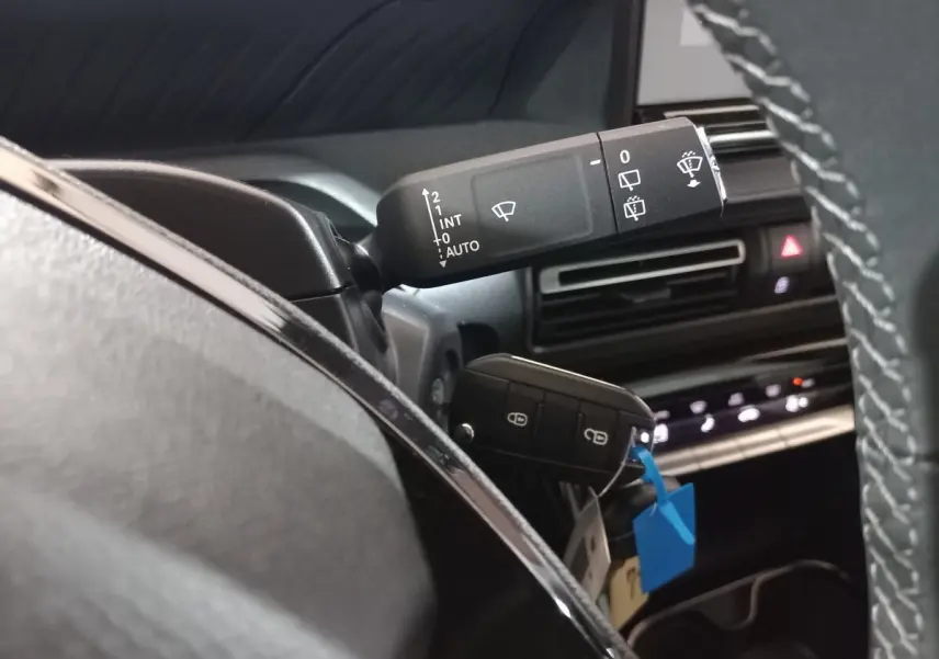 Gros plan intérieur sur la commande d'essuie-glace et clé dans le contact d'une Citroën C3 hybride 2025, tableau de bord noir.