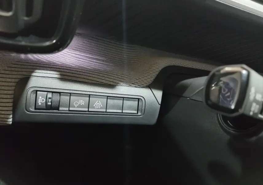 Gros plan sur les commandes de réglage des phares et aides à la conduite dans le tableau de bord d’une Citroën C3 hybride gris foncé.