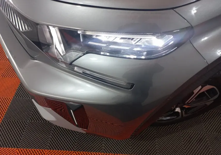 Gros plan sur le phare avant droit d'une Citroën C3 hybride gris foncé 2025, avec partie de la roue visible.