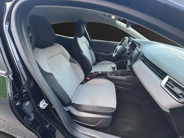 Vue intérieure côté gauche de la Renault Clio V noire, montrant les sièges gris à motif 3D et la console centrale avec boîte manuelle.