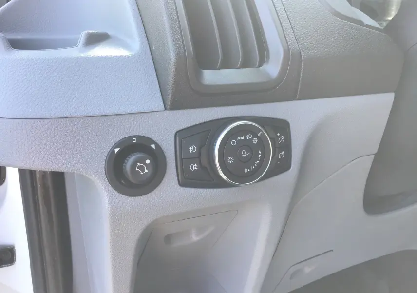 Vue rapprochée des commandes d’éclairage sur la planche de bord grise du Ford Transit Châssis Cabine blanc.