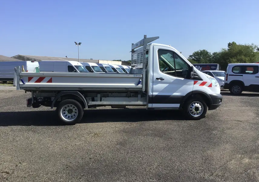 Profil côté gauche d'un Ford Transit Chassis Cabine blanc avec benne, marquages rouges et grilles métalliques arrière.