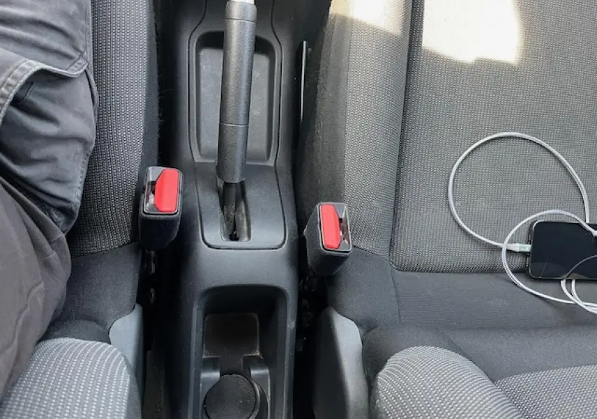 Vue plongeante sur la console centrale et les sièges noirs d'une Citroën C3 2023 avec frein à main manuel et smartphone connecté.