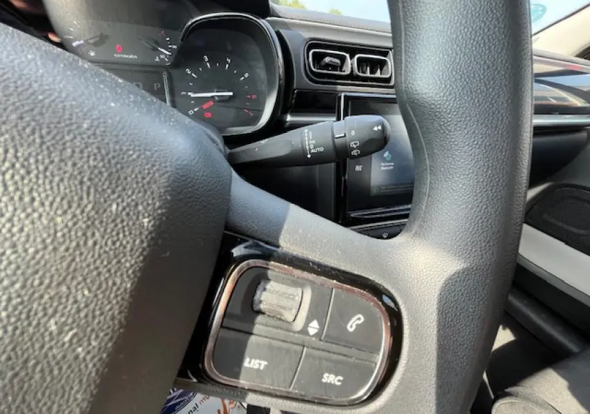 Gros plan sur les commandes audio au volant d'une Citroën C3 noire de 2023, avec tableau de bord et écran tactile en arrière-plan.