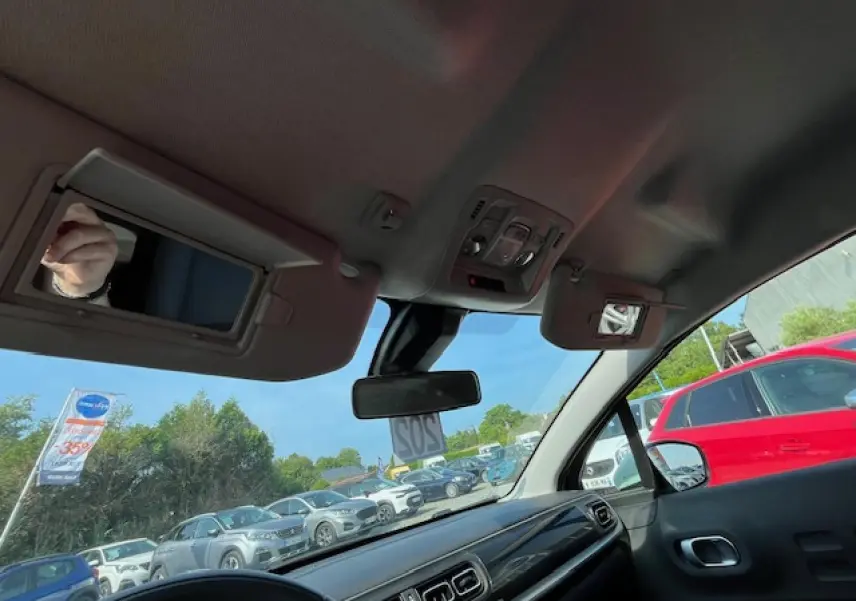 Vue intérieure avant de la Citroën C3 noire 2023, montrant tableau de bord et pare-soleils avec miroirs ouverts.