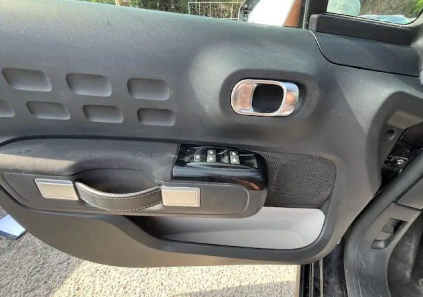 Intérieur côté gauche de la porte avant d'une Citroën C3 noire 2023, avec commandes de vitres et poignée design.
