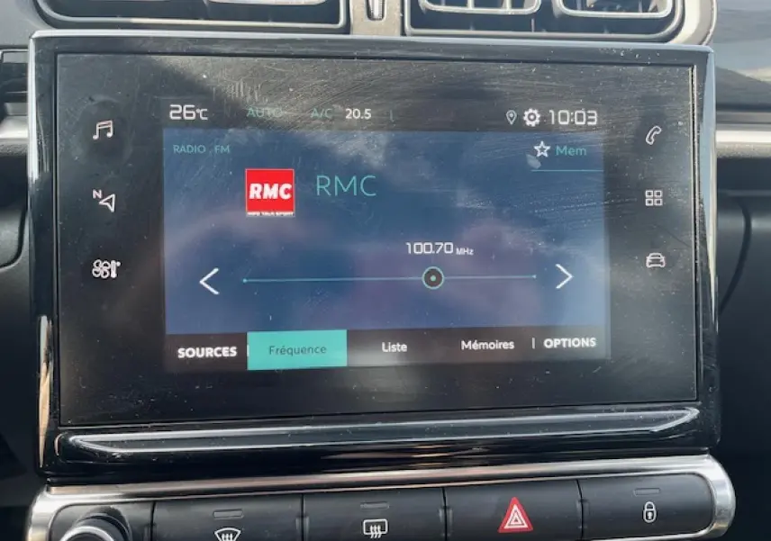 Écran tactile central de la Citroën C3 noire 2023 affichant la radio RMC à 100,7 MHz en vue frontale rapprochée.