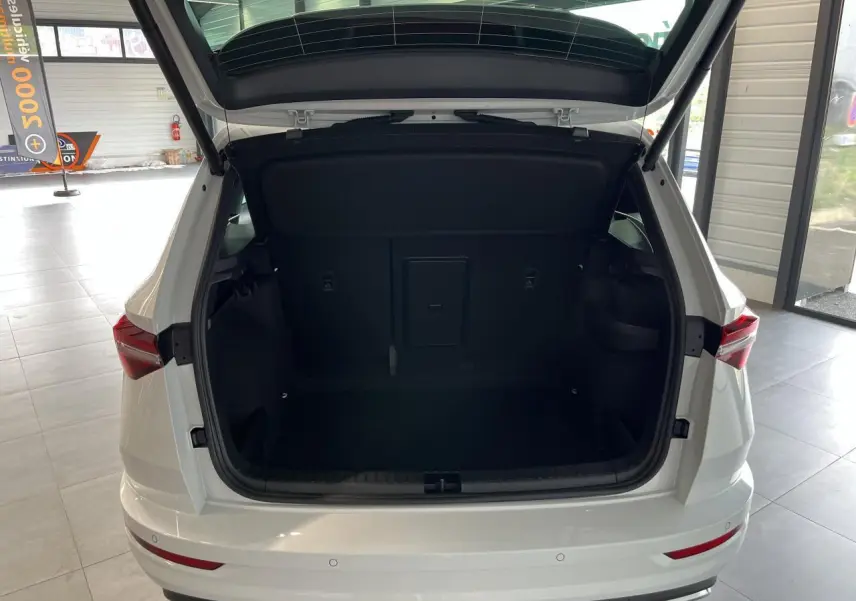 Coffre ouvert d'un SUV SKODA KAROQ blanc 2025 vu de l'arrière, montrant l'espace de chargement intérieur noir.