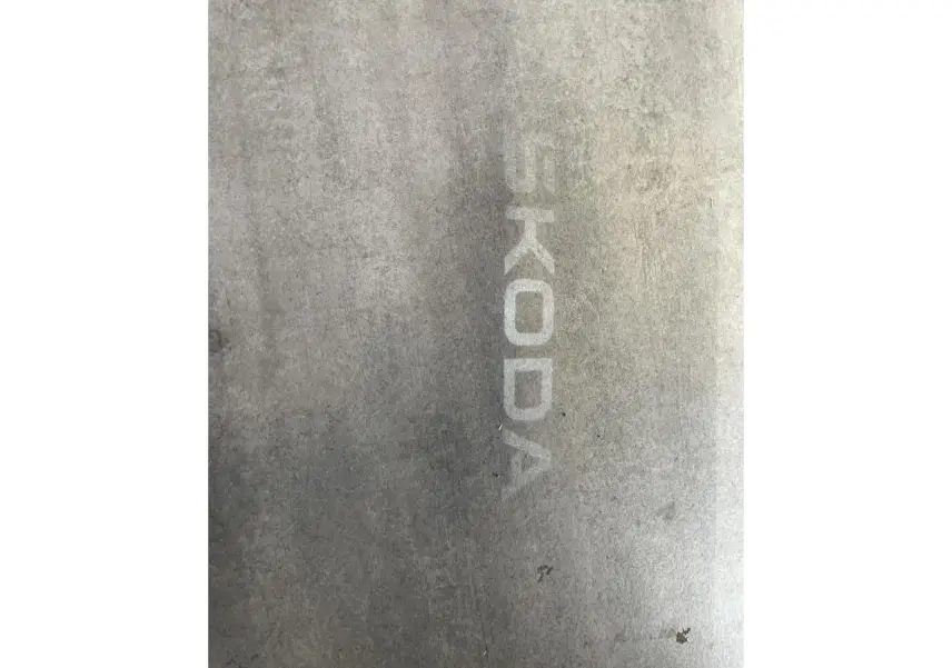 Projection lumineuse du logo SKODA au sol, visible à côté d'un véhicule blanc, angle latéral droit.