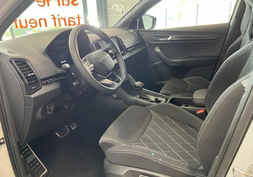 Intérieur avant droit du Skoda Karoq blanc 2025 avec sièges SportLine noirs et tableau de bord moderne.