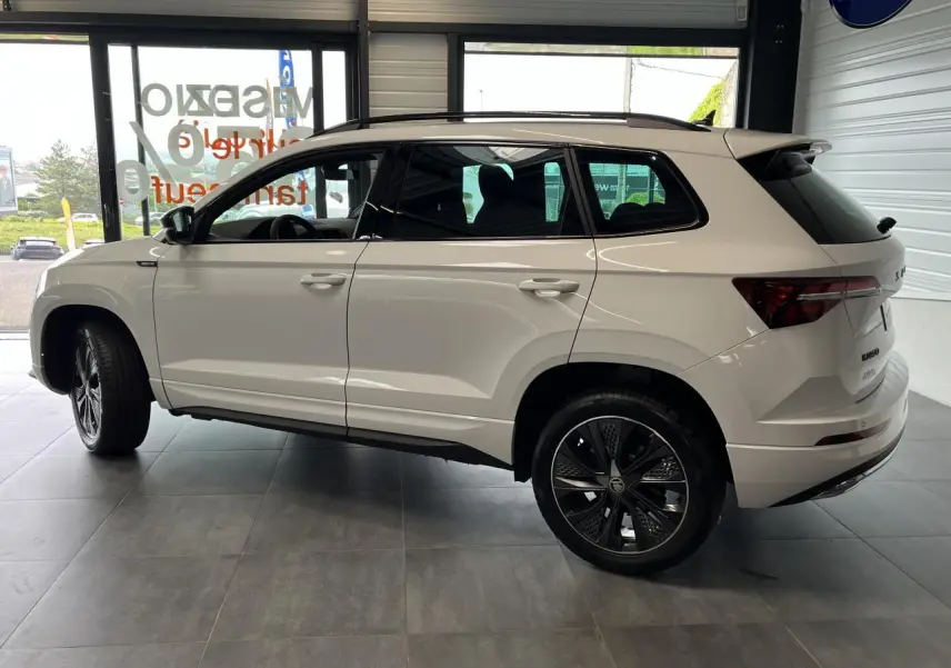 Vue latérale droite du SUV blanc SKODA KAROQ 1.5 TSI Sportline avec jantes alliage noires et vitres teintées.
