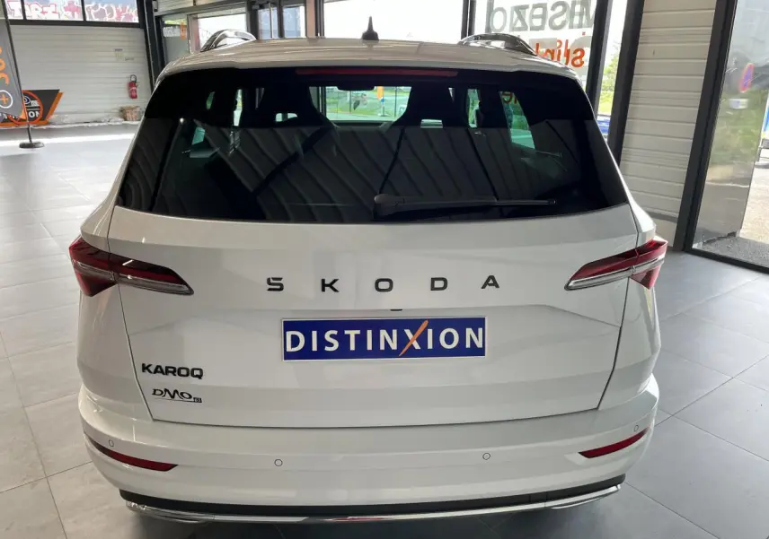 Vue arrière d'un SUV SKODA KAROQ blanc avec logo SKODA en lettres espacées et feux arrière LED fins.