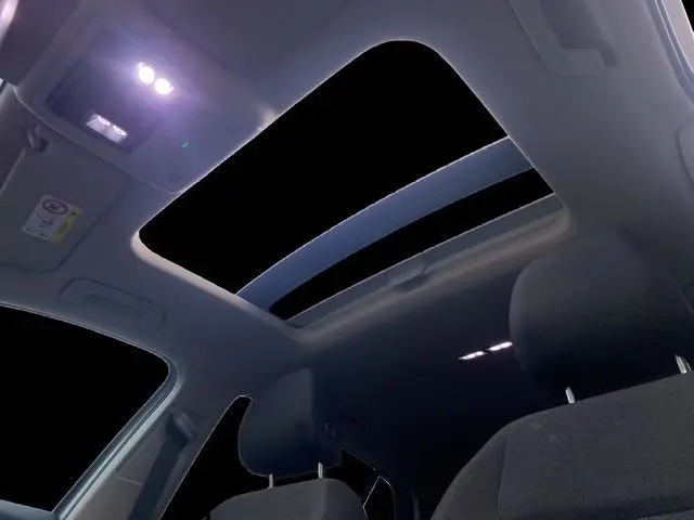 Vue intérieure nocturne du toit panoramique ouvrant de la Volkswagen Golf VIII gris argent, avec sièges avant en tissu noir.