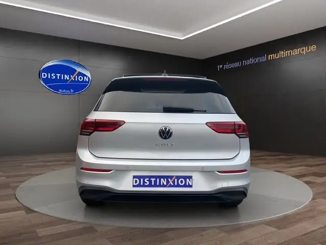 Vue arrière d'une Volkswagen Golf VIII gris argent avec vitres surteintées et toit panoramique en intérieur showroom.