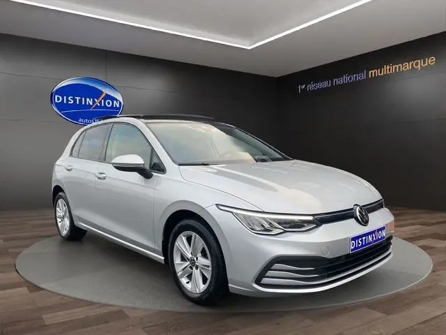 Volkswagen Golf VIII gris argent vue 3/4 avant droit en intérieur avec toit panoramique ouvrant et vitres surteintées.