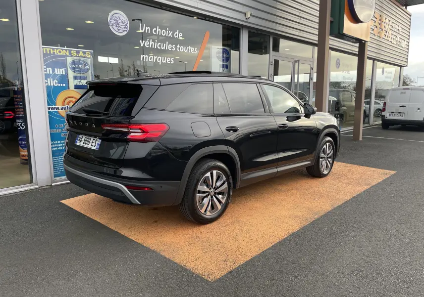 Vue 3/4 arrière droite d'un Skoda Kodiaq noir métal 2024 garé devant un showroom avec vitres teintées et jantes alliage.