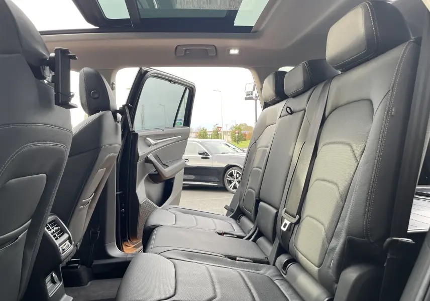 Vue intérieure sur la banquette arrière en cuir noir du Skoda Kodiaq 2024, porte arrière gauche ouverte et toit panoramique visible.