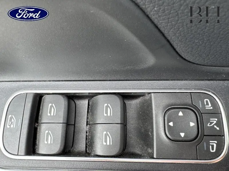 Gros plan sur les commandes de lève-vitres et rétroviseurs d'une Mercedes GLA 250 e bleu denim métallisé, côté gauche.