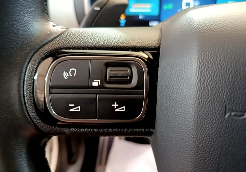 Gros plan sur les commandes gauche du volant cuir du Citroën C5 Aircross Hybrid blanc, boutons multifonctions visibles.