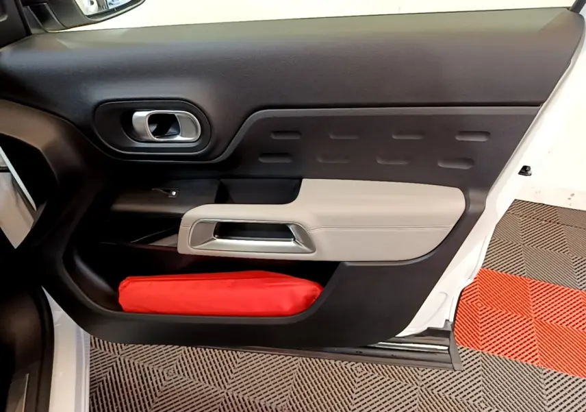 Vue intérieure côté gauche de la porte avant blanche du Citroën C5 Aircross avec garniture noire et beige et rangement rouge.