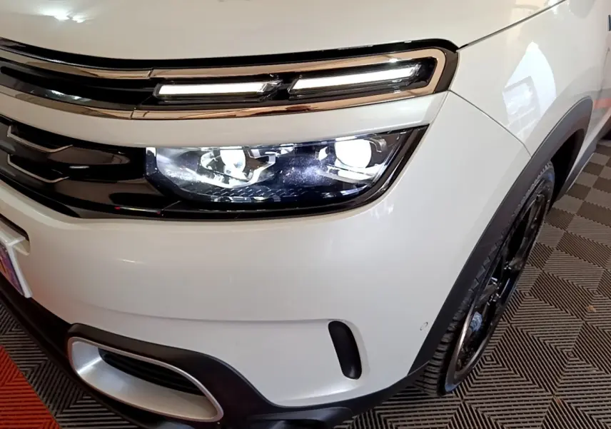 Gros plan sur l'avant droit blanc du Citroën C5 Aircross Hybrid avec phares LED allumés et jante noire visible.