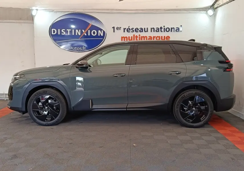 Vue de profil côté gauche d'un Citroën C5 hybride vert avec jantes noires et toit noir dans un showroom.