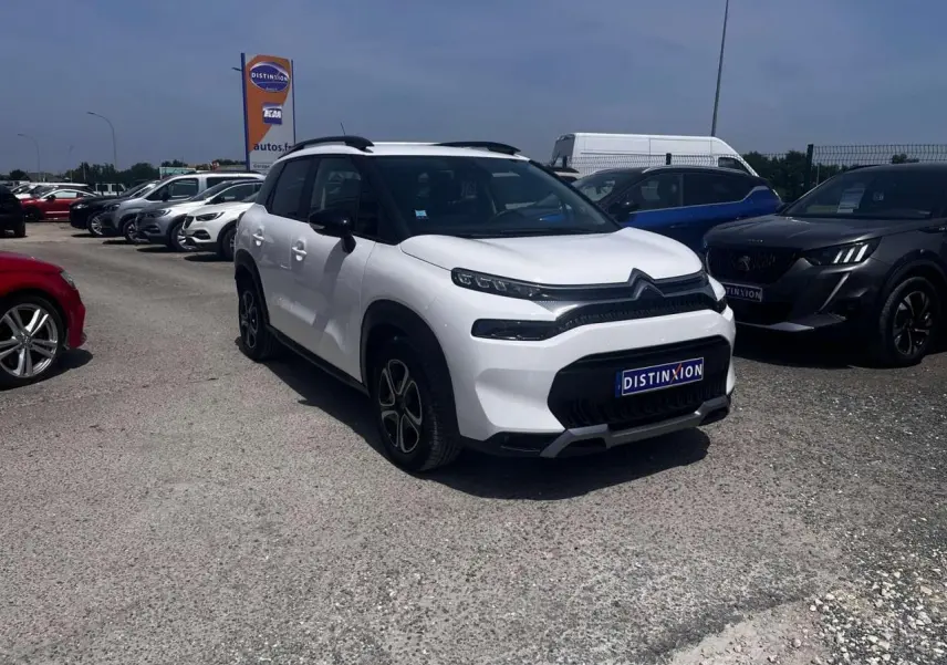 Citroën C3 Aircross blanc banquise en 3/4 avant droit avec barres de toit noir brillant sur parking.