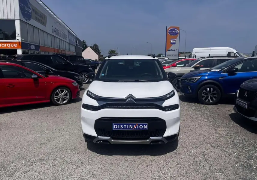 Vue avant d'un Citroën C3 Aircross blanc banquise avec calandre noire et barres de toit noires sur parking.