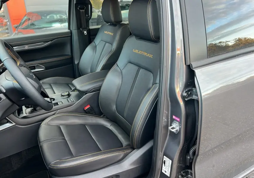 Vue intérieure côté conducteur du Ford Ranger 3.0 V6 240 Wildtrak Plus 2025 en gris carbone, sièges cuir noirs avec surpiqûres jaunes Wildtrak.