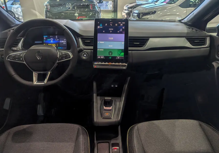 Vue intérieure frontale du tableau de bord du Renault Captur E-TECH 2025 avec écran tactile vertical et volant multifonction noir.