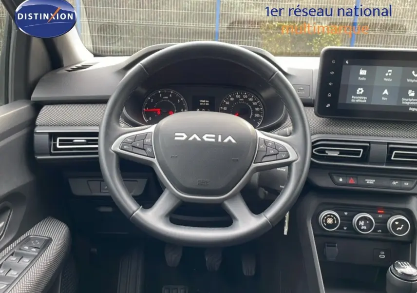 Vue intérieure centrée sur le volant DACIA d'un Jogger 2025, avec tableau de bord et écran tactile en arrière-plan.