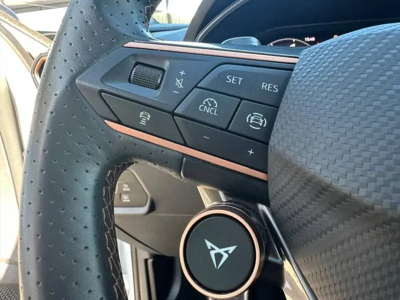 Gros plan sur le volant en cuir perforé du CUPRA Formentor blanc Nevada, avec commandes multifonctions et logo distinctif central.