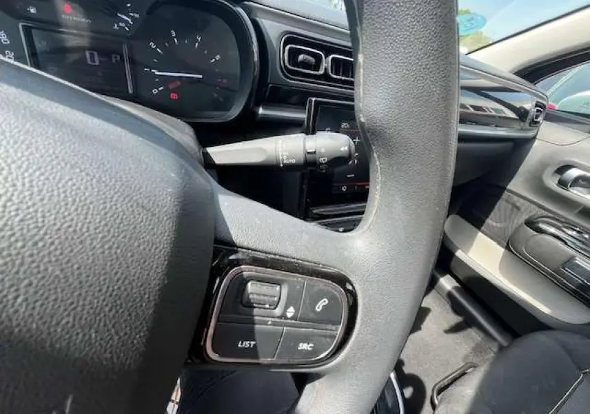 Vue rapprochée du volant noir de la Citroën C3 2023, avec commandes audio et tableau de bord en arrière-plan.