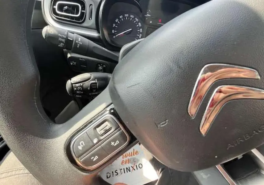 Gros plan sur le volant noir de la Citroën C3 2023 avec commandes audio intégrées et logo chromé visible.