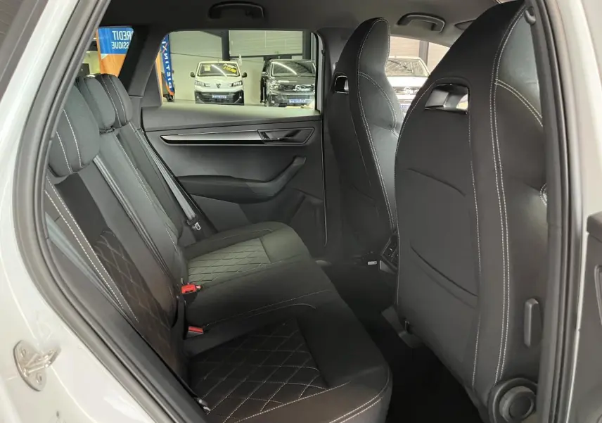 Vue côté gauche sur l'intérieur arrière noir avec surpiqûres blanches du Skoda Karoq blanc 2025 Sportline