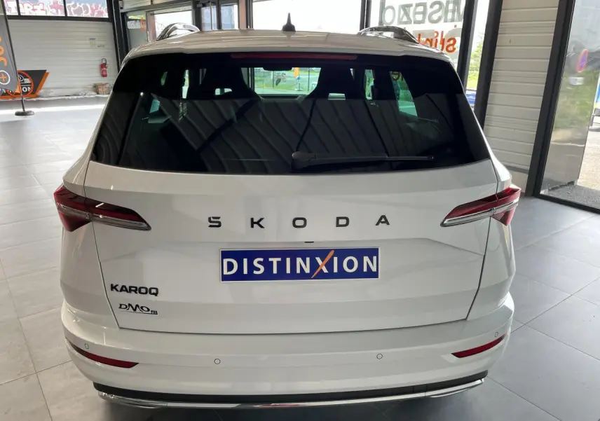 Vue arrière d'un SUV SKODA KAROQ blanc 2025 avec hayon électrique et feux arrière LED en intérieur showroom.