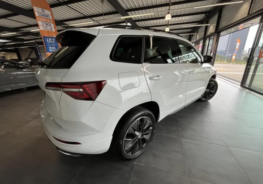 Vue 3/4 arrière droite du SUV blanc SKODA KAROQ 2025 Sportline avec jantes alliage noires et vitres teintées.