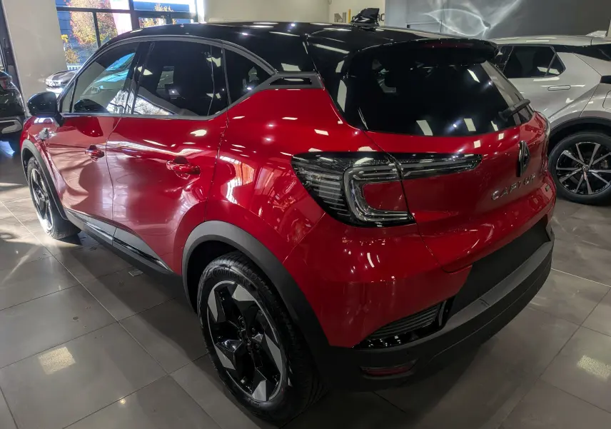 Renault Captur E-TECH hybride rouge Flamme avec toit noir, vue 3/4 arrière droit en showroom lumineux.