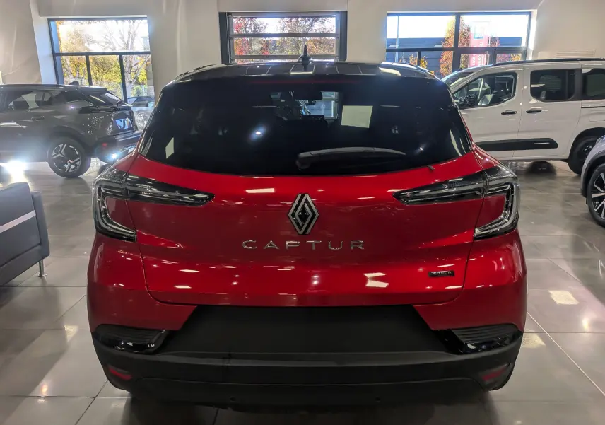 Vue arrière du Renault Captur E-TECH rouge Flamme avec toit noir, en intérieur d'exposition lumineuse.
