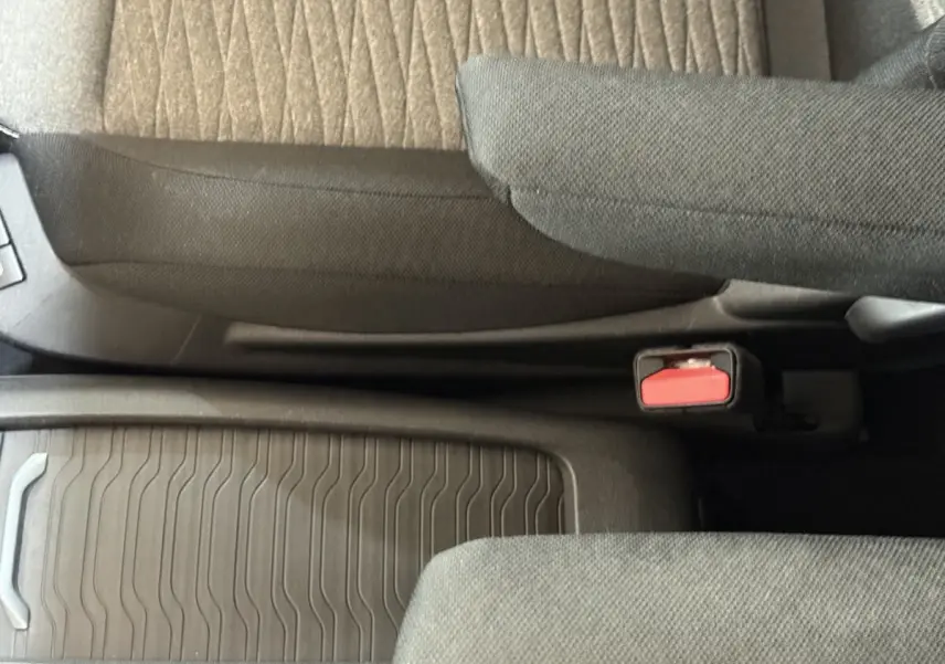 Vue intérieure rapprochée du siège conducteur et de la console centrale avec tissu gris et ceinture de sécurité rouge.
