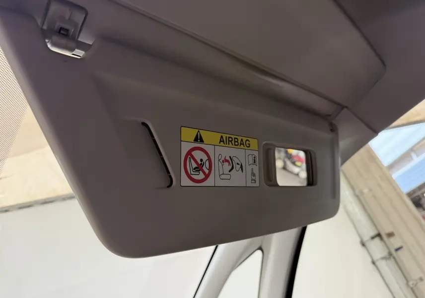 Pare-soleil côté conducteur gris clair avec avertissement airbag et petit miroir intégré, vue intérieure rapprochée.