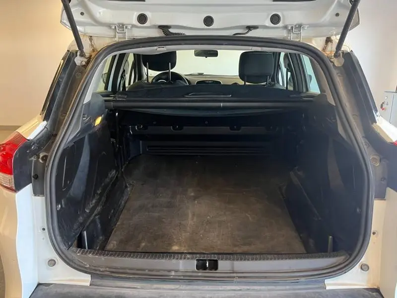 Coffre ouvert vu de l'arrière d'une Renault Clio Estate blanc glacier, montrant l'espace de chargement vide et la tablette cache-bagages.