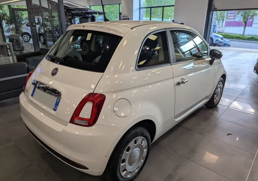 Vue 3/4 arrière droite d'une FIAT 500 blanche Bossanova dans un showroom, avec jantes acier et rétroviseurs noirs.