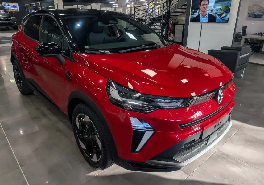Renault Captur E-Tech 2025 rouge flamme avec toit noir, vue 3/4 avant en showroom lumineux.