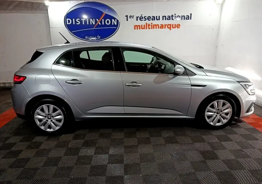Profil droit d'une Renault Mégane Business Blue dCi 115 EDC gris clair, stationnée en intérieur sur sol damier.