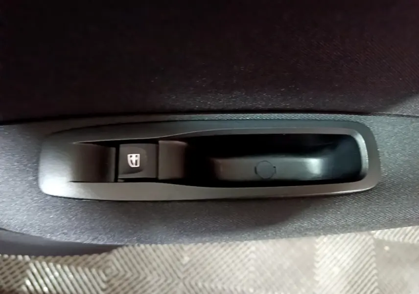 Gros plan sur le bouton de commande de lève-vitre noir dans l'accoudoir intérieur d'une Renault Mégane Business Blue dCi 115 EDC gris clair.